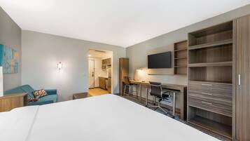 Quarto de hotel com uma cama grande, uma escrivaninha com cadeira, televisão na parede e um guarda-roupa.