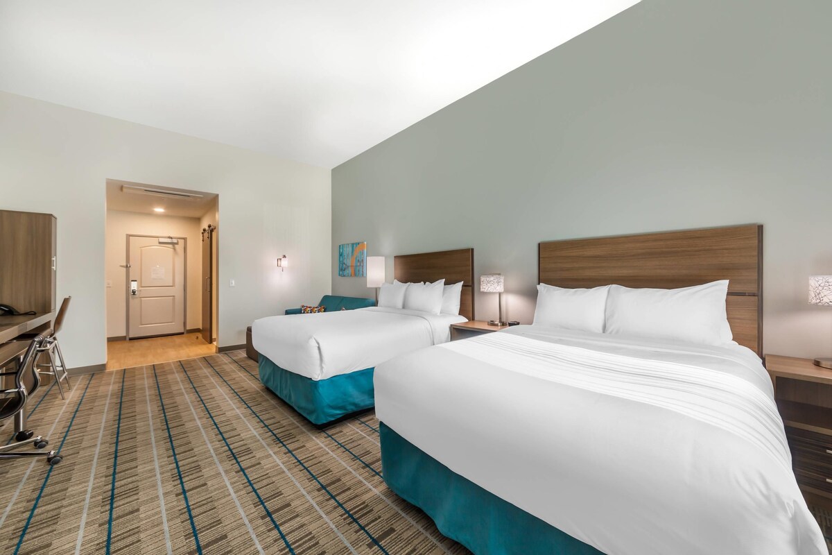 A hotel room with two beds, a desk, and a chair.