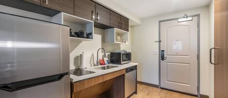 A modern kitchen with a stainless steel refrigerator, a microwave, and a dishwasher. There are wooden cabinets and a countertop with a sink.