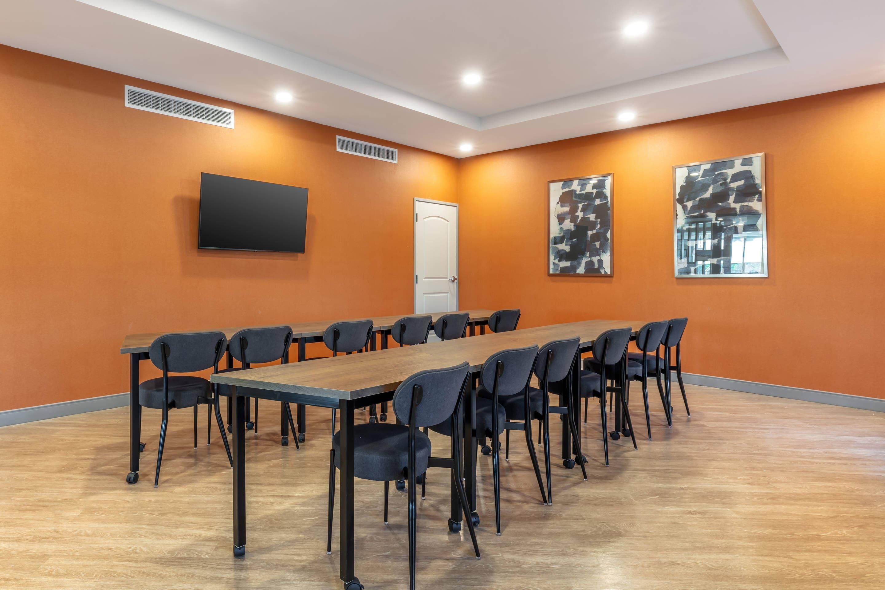 Una sala conferenze con un lungo tavolo, sedie, un televisore a schermo piatto e due dipinti astratti alle pareti.