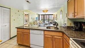 A kitchen with wooden cabinets, a built-in dishwasher, a granite countertop, and a window overlooking a cityscape. - Sea Watch 119 by Seaside Vacations & Sales (Ocean City)