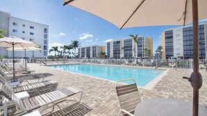 A poolside area with lounge chairs and umbrellas, surrounded by a pool and buildings in the background. - Great Amenities - Canal Views - Walk to Beach - 2BR Casa Marina II #431 (Fort Myers Beach)