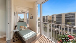 A balcony with a bed, a small table, and a ceiling fan. - Great Amenities - Canal Views - Walk to Beach - 2BR Casa Marina II #431 (Fort Myers Beach)