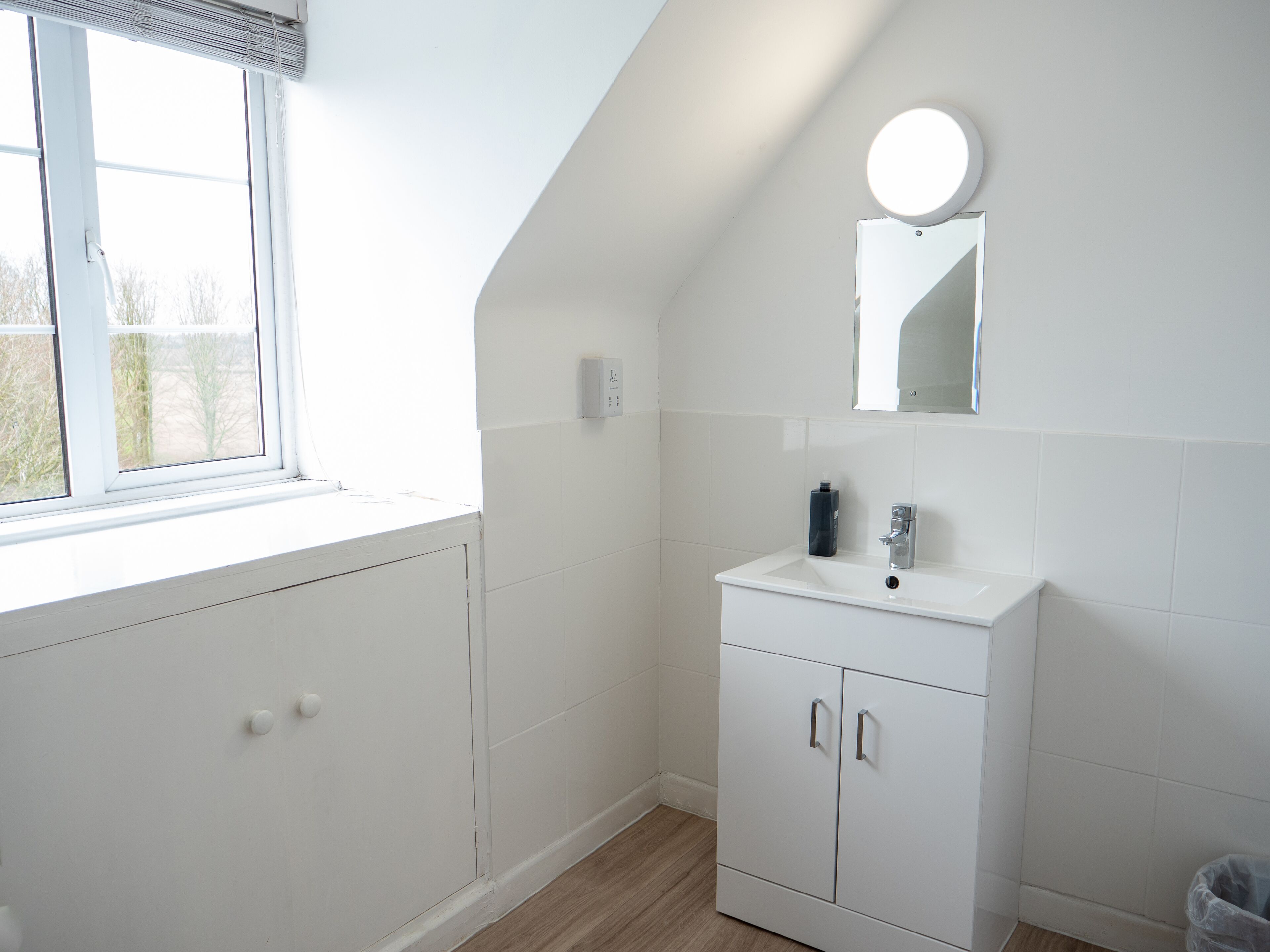 A modern bathroom with a white sink, mirror, and cabinets.