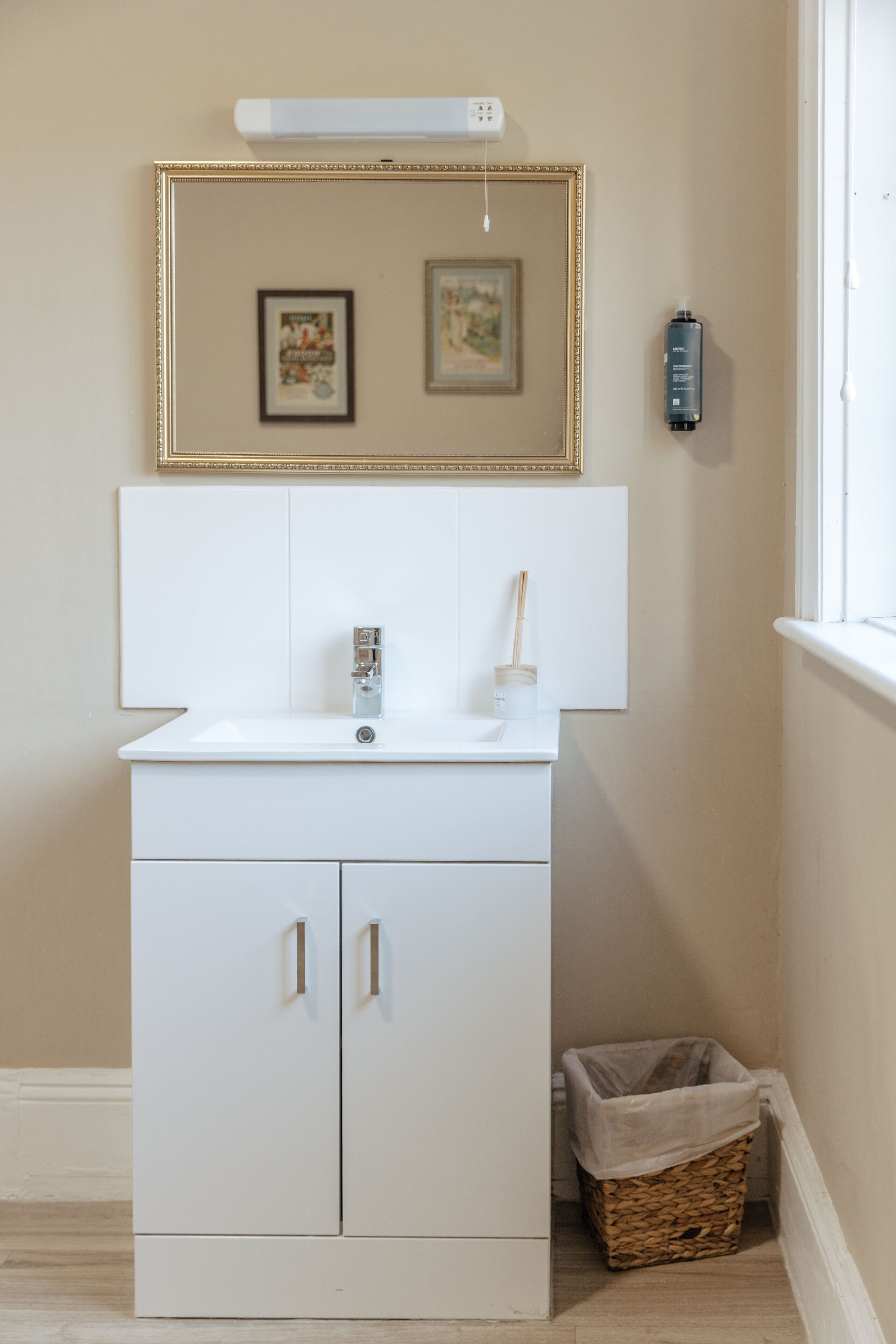 A white bathroom vanity with a mirror, a sink, and a small trash bin.