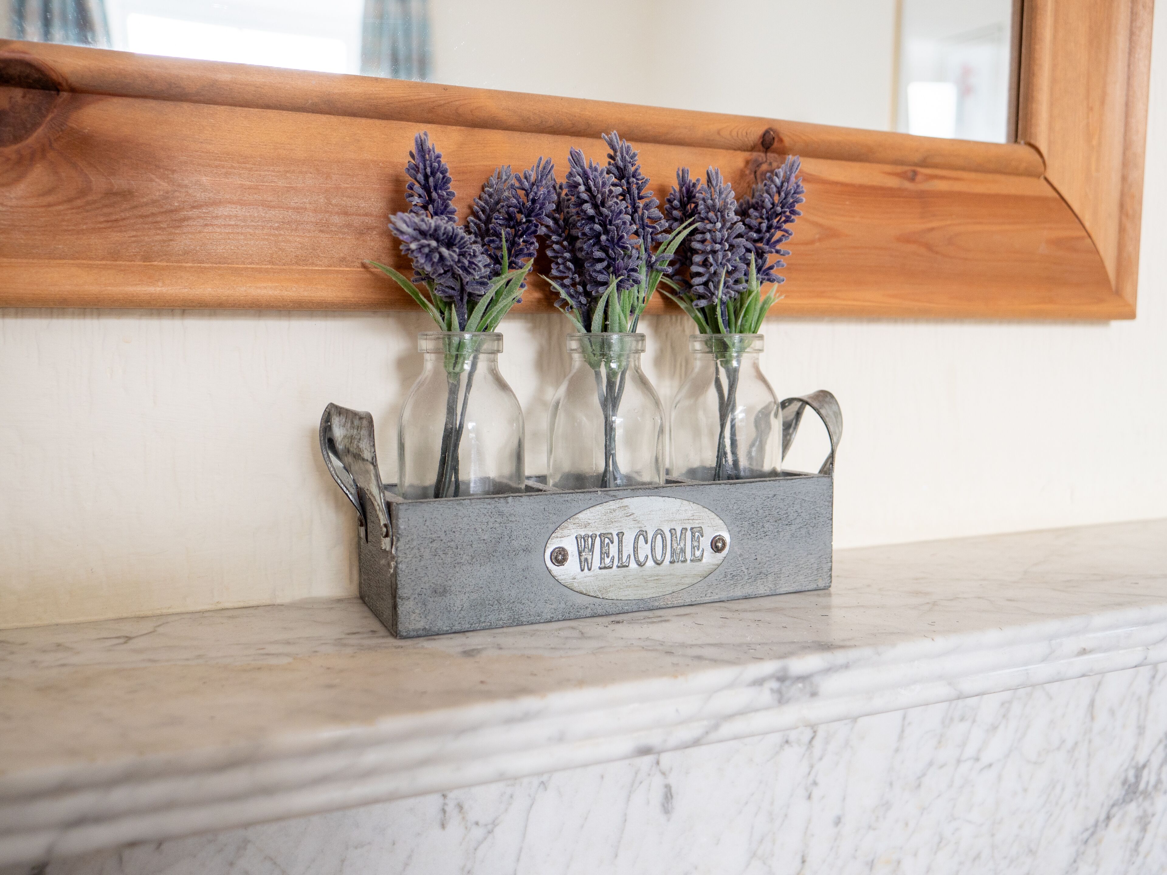 Un cartello di benvenuto con fiori di lavanda in bottiglie di vetro su un ripiano in marmo.