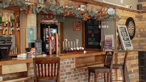 A bar area with wooden bar counter, two stools, and various bar tools. - The Horton Inn (Wimborne)