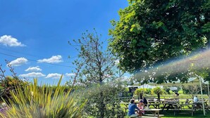 A picnic area with wooden tables and benches, surrounded by lush greenery and trees. - The Horton Inn (Wimborne)