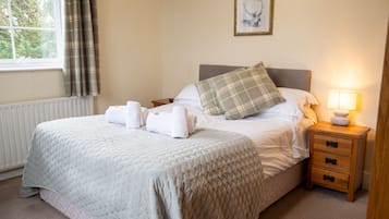 Una cama bien hecha con una colcha acolchada, dos almohadas y dos toallas dobladas al lado. Hay una mesita de noche con una lámpara y un cuadro enmarcado en la pared sobre la cama.