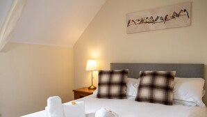 A neatly made bed with white linens and two rolled towels, a bedside lamp, and a painting of birds on the wall. - The Horton Inn (Wimborne)