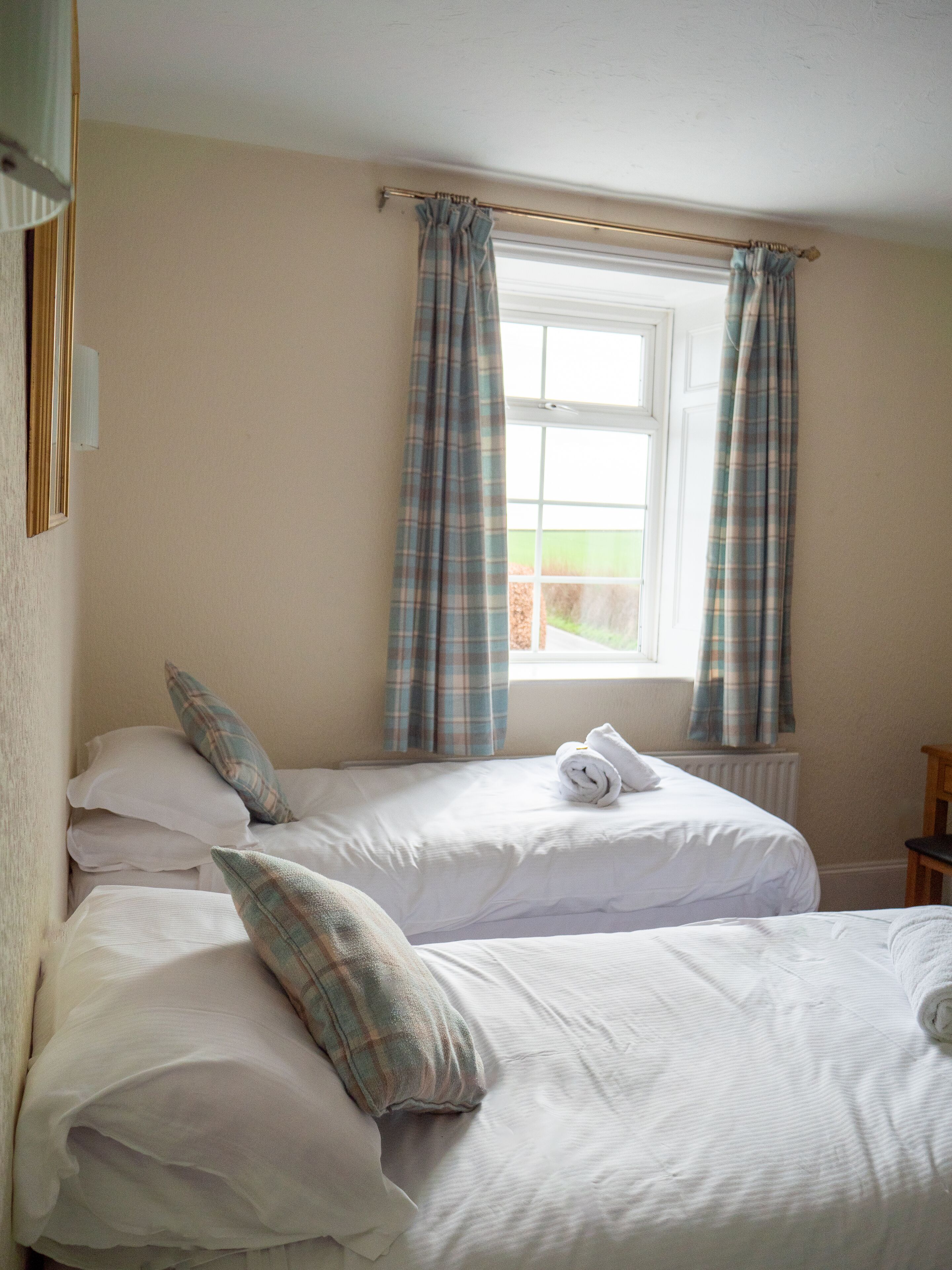 A bedroom with two beds, plaid curtains, a window, and a radiator.