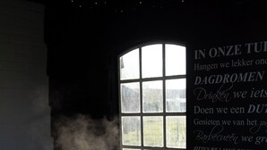 Una persona en un jacuzzi con vapor saliendo, una ventana y una pared con texto en un idioma extranjero.