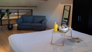 Un dormitorio con una cama, una mesita con cosas para el desayuno, un sofá gris y un espejo grande.