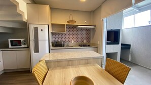 Cocina compacta con refrigerador, microondas y estufa. Hay una mesa de comedor con sillas y una pequeña isla.