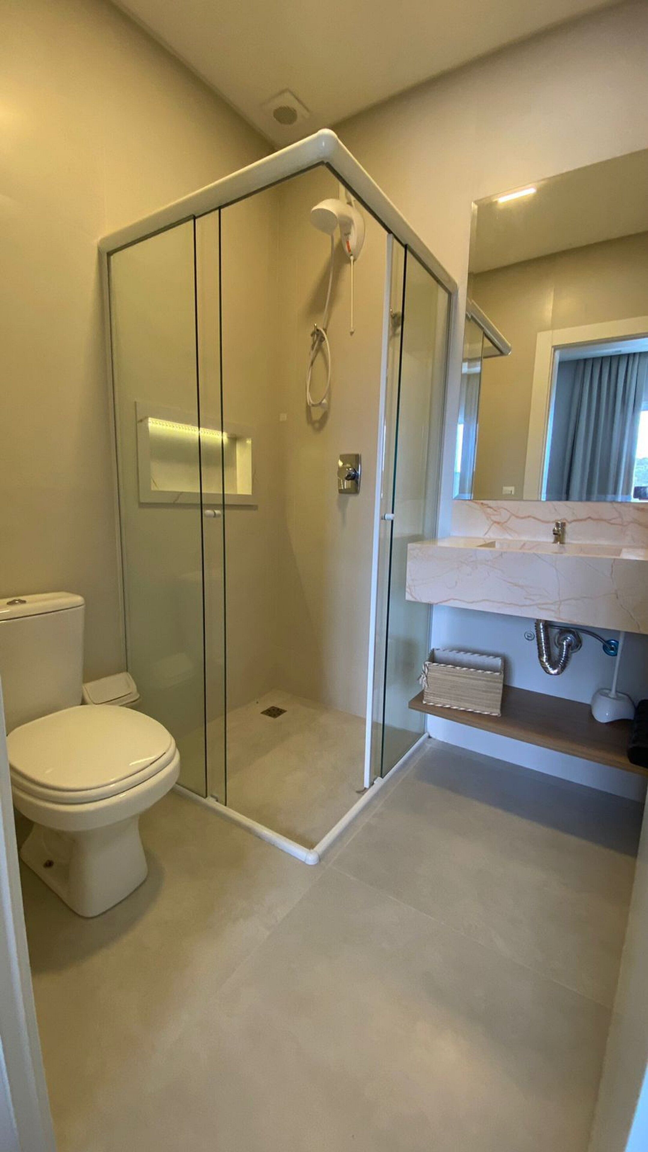 A modern bathroom with a glass-enclosed shower, a toilet, and a vanity with a marble countertop.