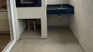 Un balcón pequeño y cerrado con una parrilla empotrada, un lavabo y un taburete.