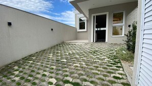 Un patio pavimentado con un diseño geométrico, una pared exterior blanca y una puerta que da a un acceso cubierto.