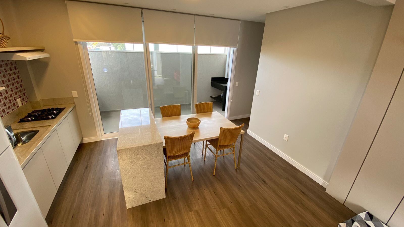 A modern kitchen with a dining area, wooden flooring, and a large sliding glass door leading to a balcony.