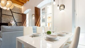 A dining area with a white table set for four, a sofa, and a stone wall with a wooden door.