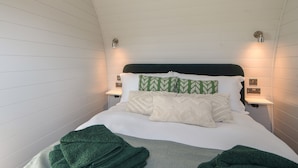 Een opgemaakt bed met groen-witte beddengoed, twee bedlampjes en een wandlamp.