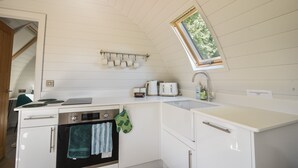 Een compacte keuken met witte kastjes, een ingebouwde oven, een kookplaat, een raam boven de spoelbak, en een klein aanrecht met een broodrooster en waterkoker.