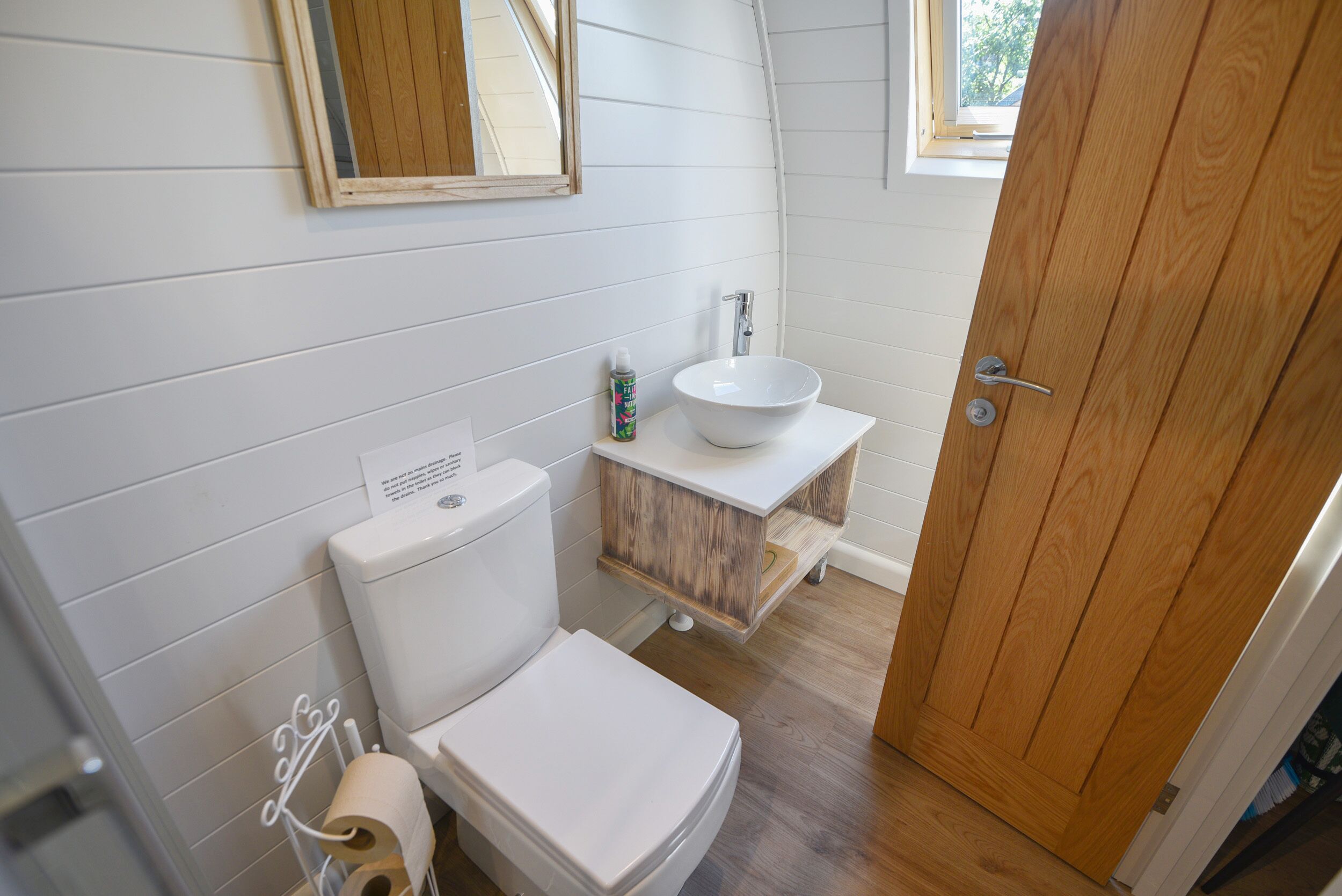 A bathroom with a white toilet, a wooden vanity with a white sink, and a wooden door.
