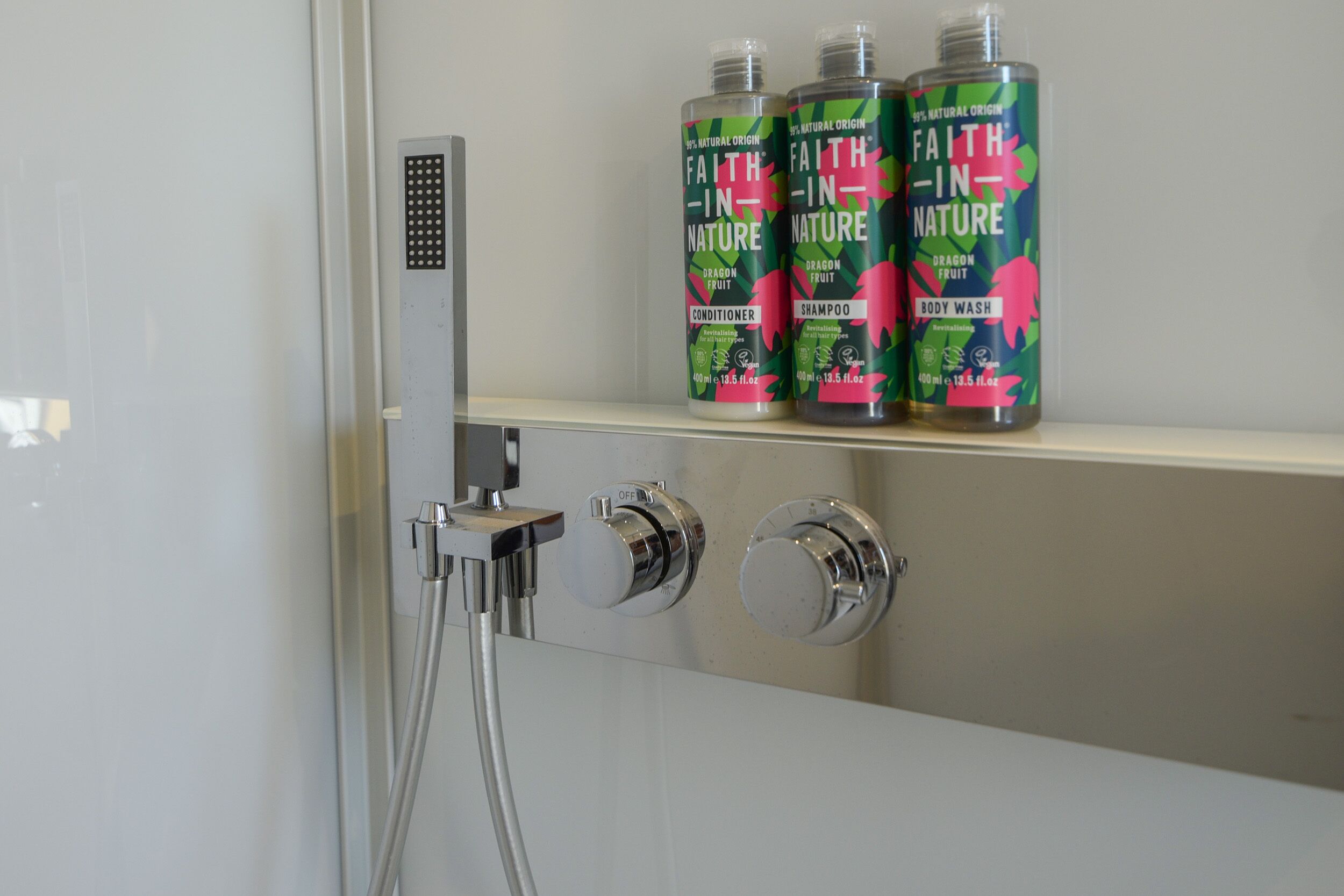 Un baño con ducha, dos botellas de jabón corporal Faith-in-Nature y un cabezal de ducha manual.
