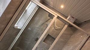 A modern bathroom with a glass-enclosed shower, marble flooring, and a white sink. - Kisa apartments (Jinja)