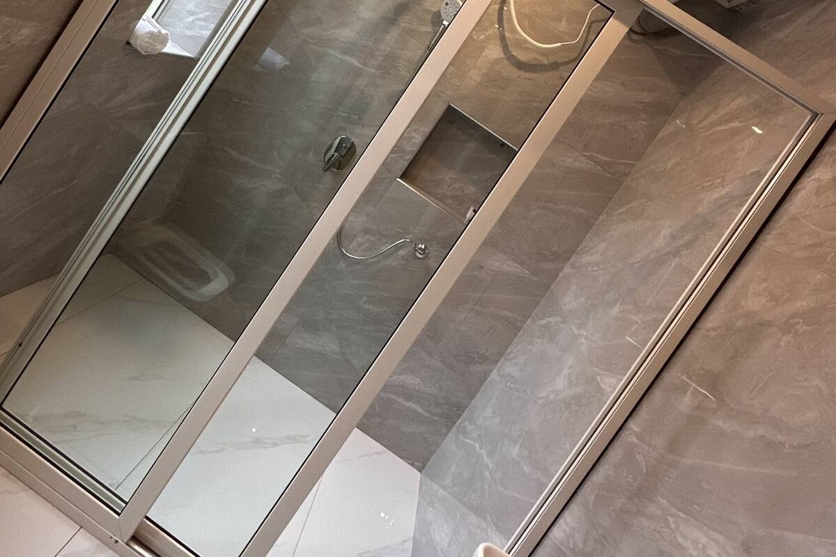 A modern bathroom with a glass-enclosed shower, marble flooring, and a white sink.