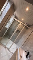 Un baño moderno con ducha envuelta en cristal, suelo de mármol y lavamanos blanco.
