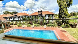 A swimming pool with a tiled deck, surrounded by lush greenery and a clear blue sky. - Kisa apartments (Jinja)