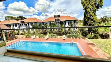 Una piscina con borde de baldosas, rodeada de abundante vegetación y un cielo azul despejado.