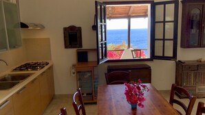 A kitchen with a view of the sea, a dining table with chairs, and a window with an open shutter. - Bluehorizon (Torre Delle Stelle (Maracalagonis))
