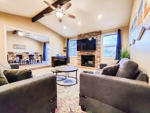 A living room with a fireplace, a ceiling fan, and a dining area in the background.