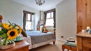 Une chambre à coucher avec un lit, une commode, une chaise, un miroir et un vase rempli de tournesols.