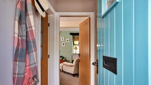 Un couloir avec une écharpe à carreaux accrochée au mur, une porte en bois et, au fond, un fauteuil beige.
