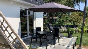 An outdoor patio with a table and chairs, a large umbrella, and a wooden deck. - Ferienhaus Janeviz 1312 (Kröpelin)