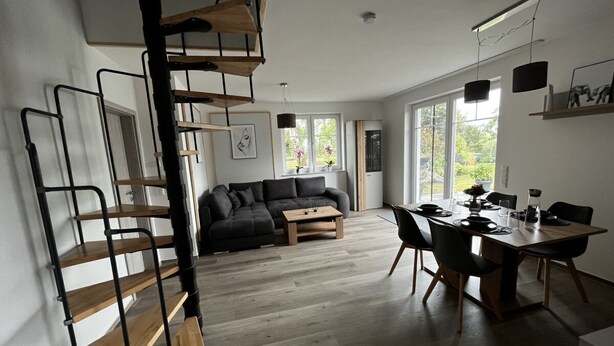 A modern interior with a spiral staircase, a sofa set, a dining table with chairs, and large windows. - Ferienhaus Janeviz 1312 (Kröpelin)