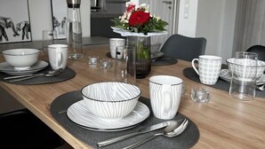 A dining table set with plates, bowls, cups, and a vase with flowers. - Ferienhaus Janeviz 1312 (Kröpelin)