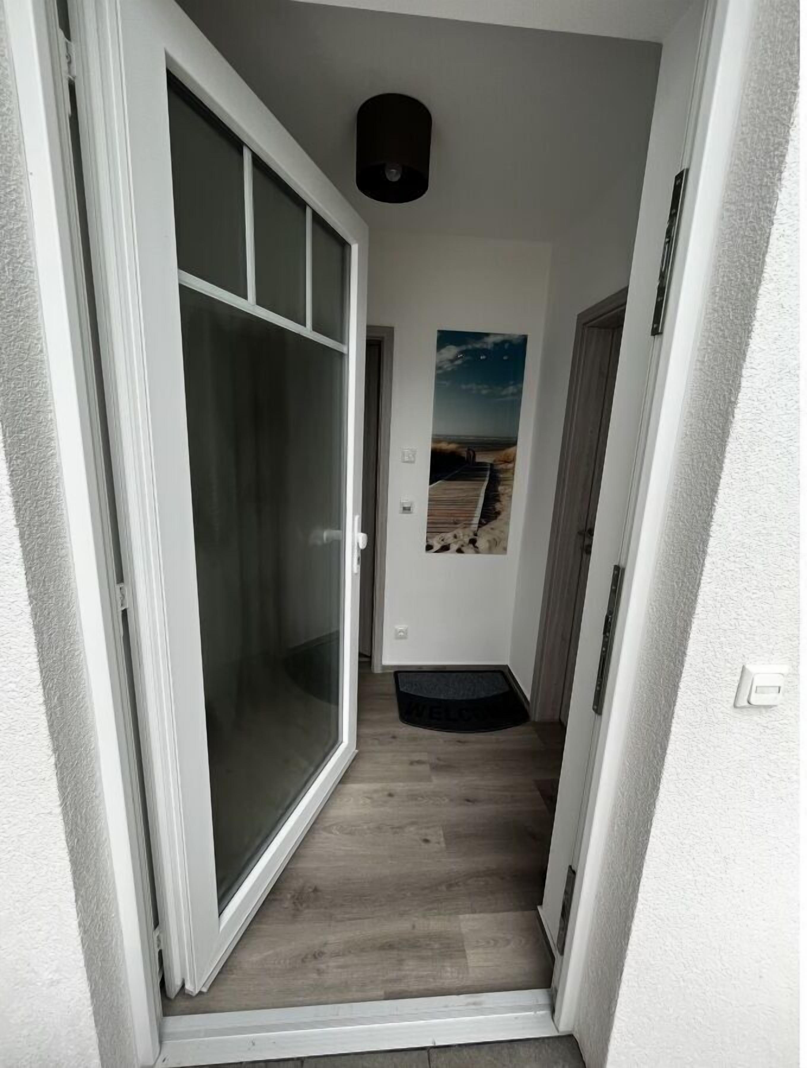 A narrow hallway with a sliding glass door leading to a room. A welcome mat is placed at the entrance.