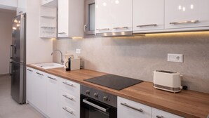 A modern kitchen with white cabinets, a stainless steel refrigerator, a wooden countertop, a toaster, and an oven. - Hosting Moments Semi Basement Apartment (Mykonos)