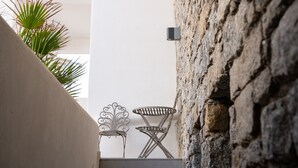 A stone wall with a metal chair and table, a potted plant, and a white wall in the background. - Hosting Moments Semi Basement Apartment (Mykonos)