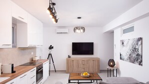 A modern kitchen with white cabinets, a wooden countertop, and a built-in oven. There is a tripod and a basket of fruit on the counter. - Hosting Moments Semi Basement Apartment (Mykonos)