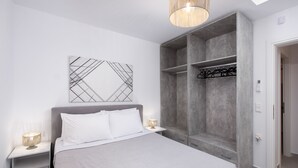 A modern bedroom with a large bed, a wardrobe, and a bedside table with a lamp. - Hosting Moments Semi Basement Apartment (Mykonos)