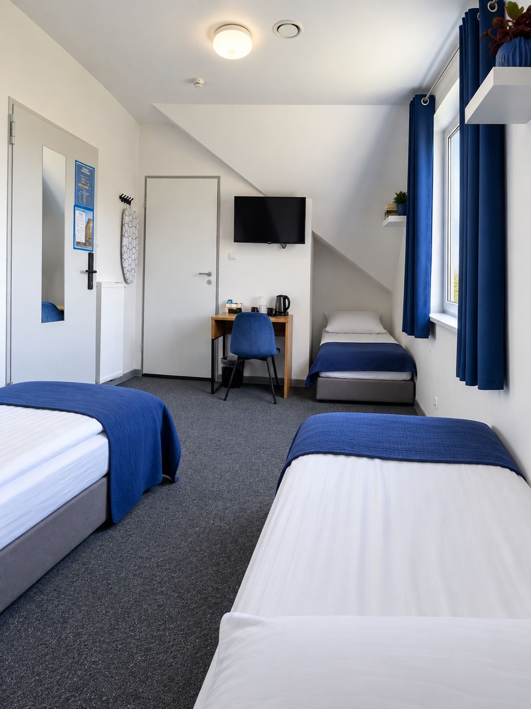 A hotel room with two beds, a desk, a TV, and a window with curtains.