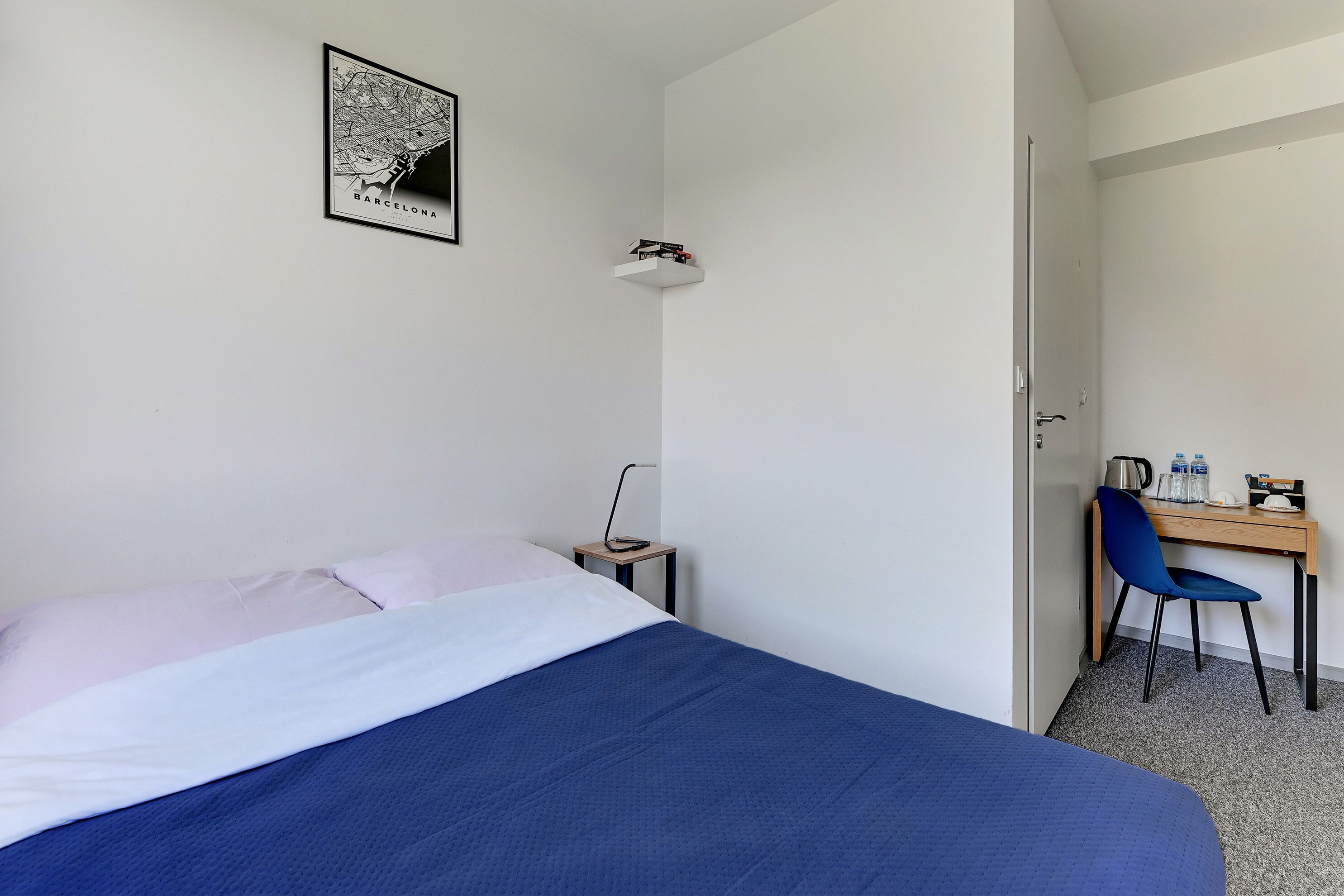 Habitación de hotel con cama, escritorio, silla, un mapa en la pared y una puerta que da a otra habitación.