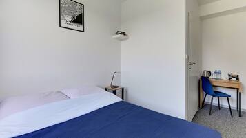 Habitación de hotel con cama, escritorio, silla, un mapa en la pared y una puerta que da a otra habitación.