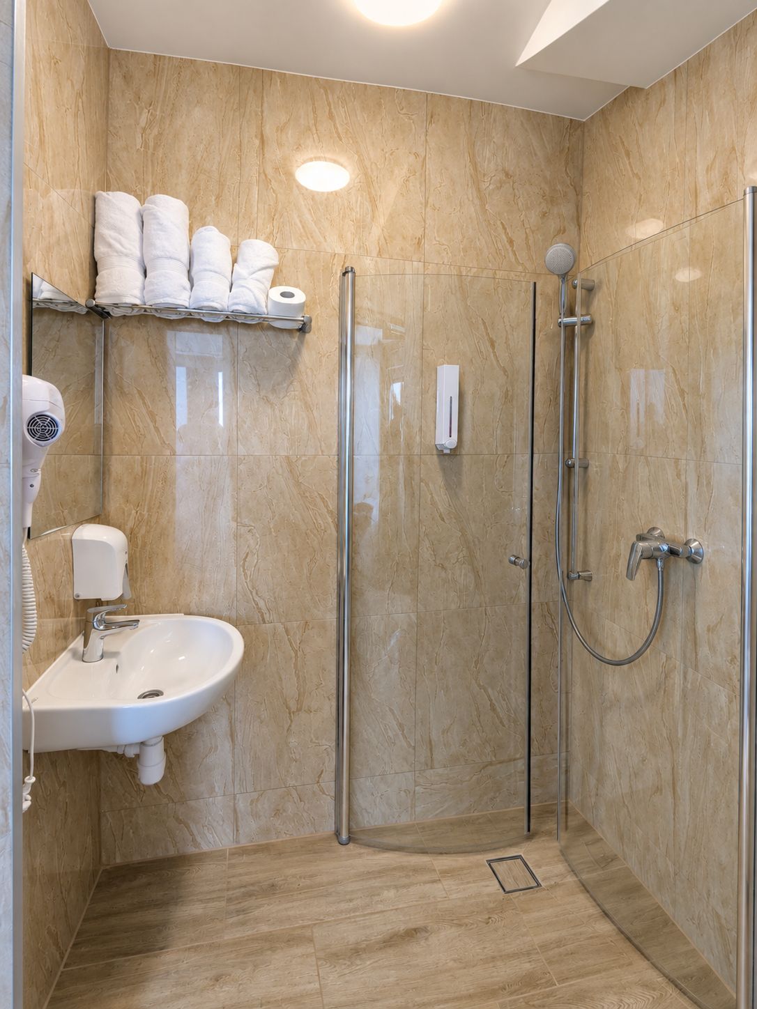 Une salle de bain moderne avec une douche en verre, un lavabo doté d’un sèche-mains et des serviettes soigneusement rangées.
