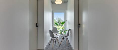 Un pasillo con una ventana, dos sillas y una mesa.