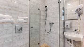 A modern bathroom with a glass-enclosed shower, a white sink, and neatly folded towels on a shelf.